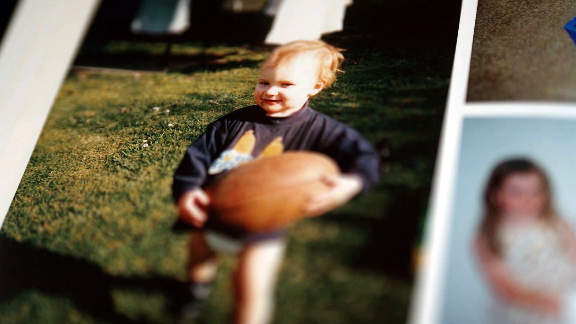 A photo in a page of a photo album of a toddler holding a football, it is large in the young boy's hands.