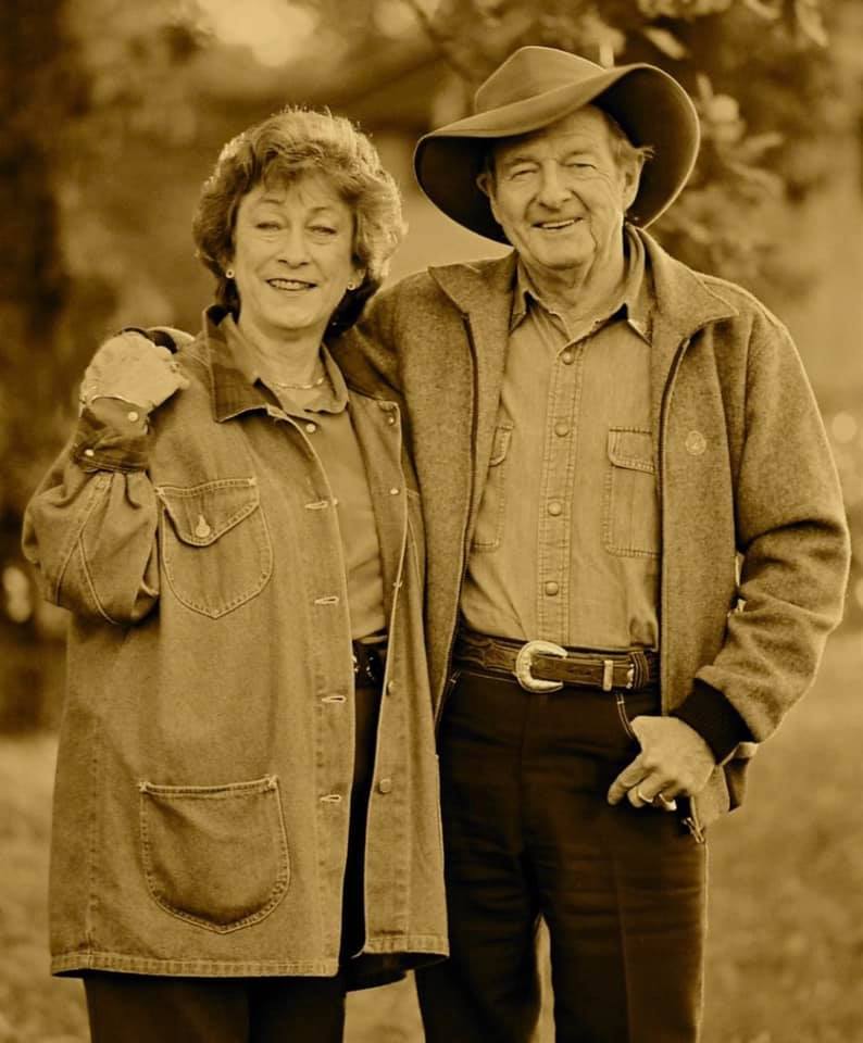 Man wearing a hat stands with arm around his wife. 