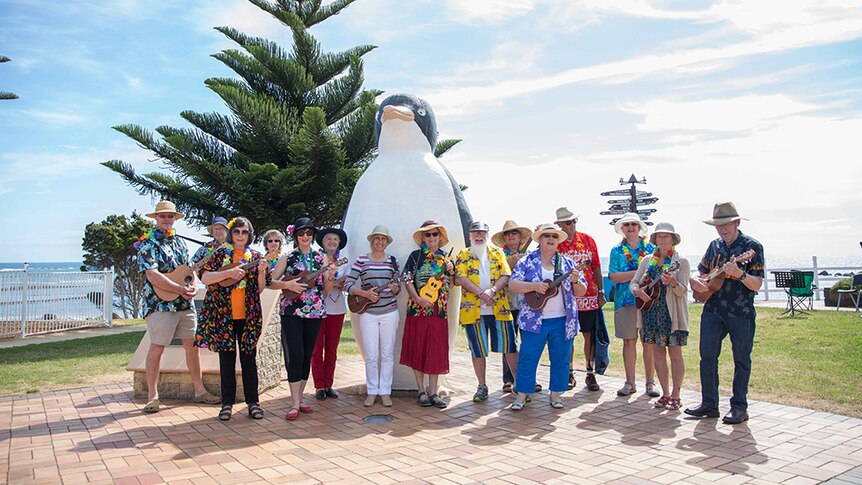 Ukulele players gather in front of a large sculpture of a Penguin.