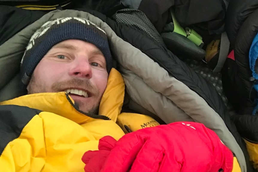 Man in yellow jacket rugged up in a sleeping bag.