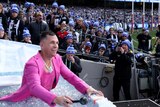 Joel Selwood in a pink suit dressed as Robbie Williams, smiles while standing in ice water at the Big Freeze at the 'G.