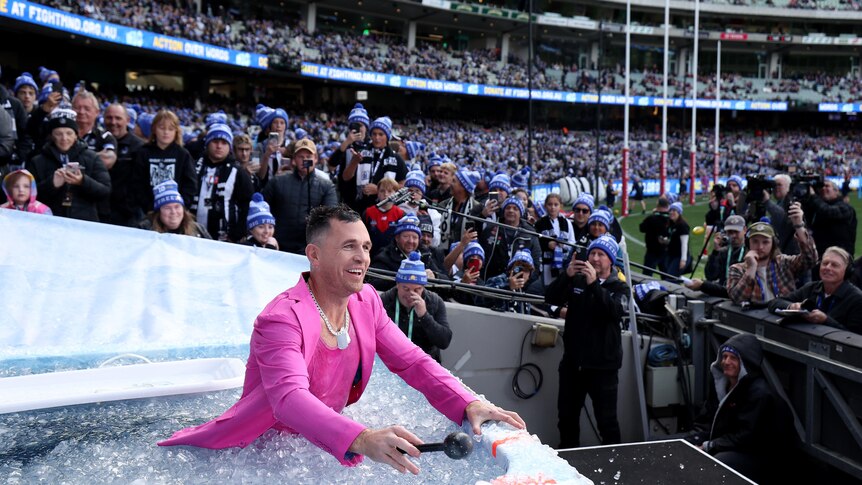 Joel Selwood in a pink suit dressed as Robbie Williams, smiles while standing in ice water at the Big Freeze at the 'G.