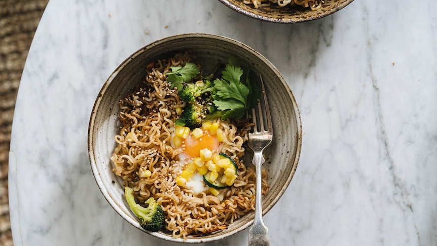 A bowl of instant ramen noodles with broccoli, corn, zucchini, coriander and egg, a fast vegetarian recipe.