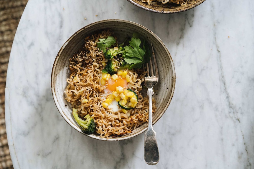 A bowl of instant ramen noodles with broccoli, corn, zucchini, coriander and egg, a fast vegetarian meal.