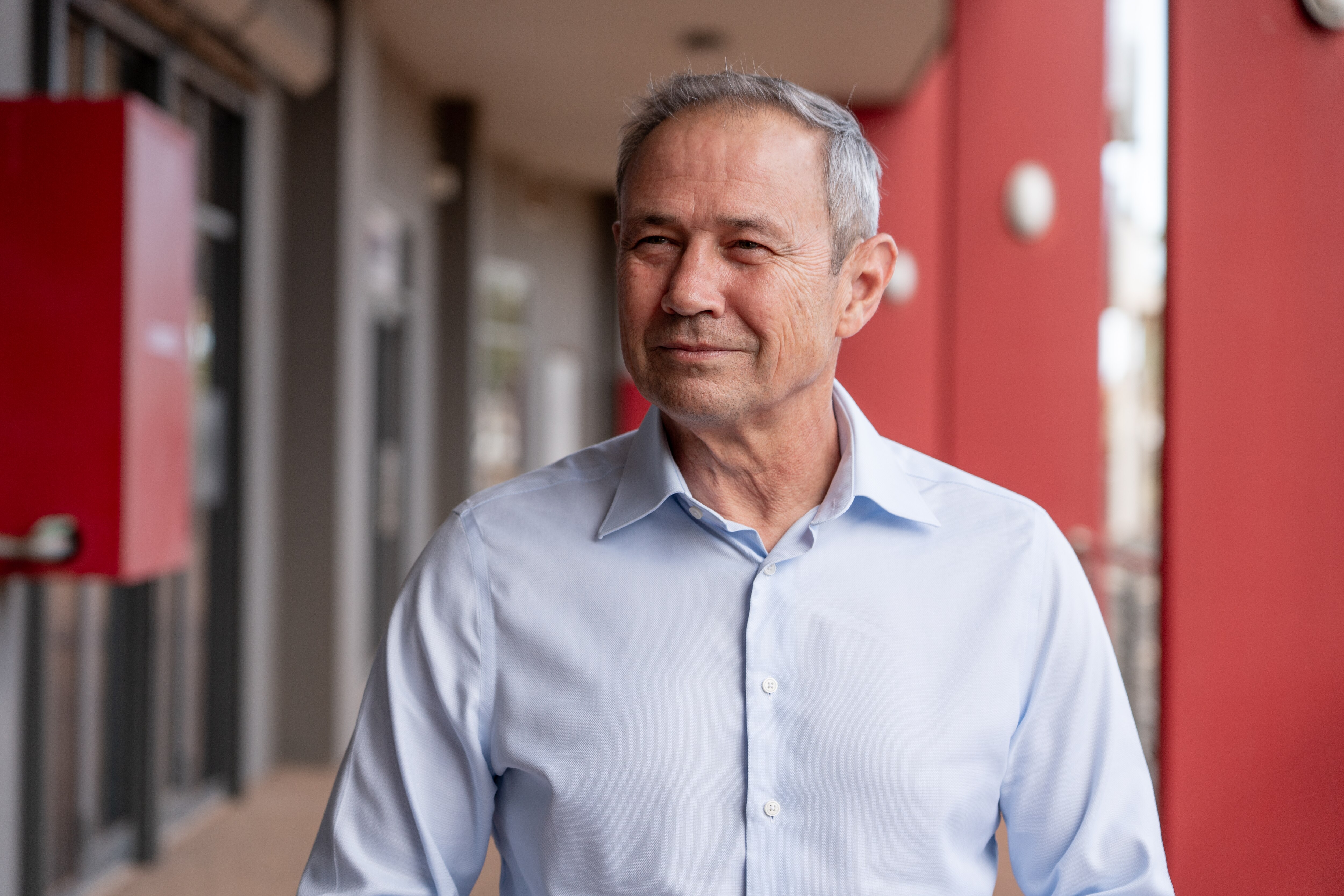 Un hombre de mediana edad con pelo corto y gris viste una camisa abotonada y se encuentra bajo el toldo de un gran edificio.