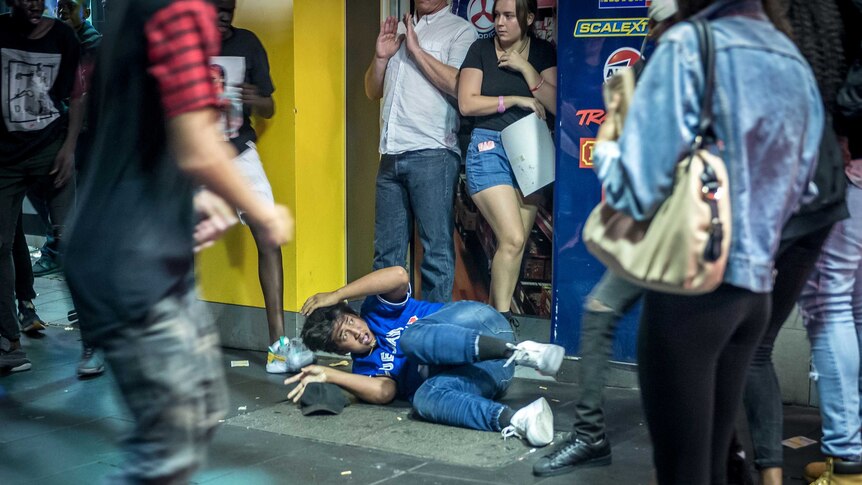 A young man lying on the ground tries to protect his head.
