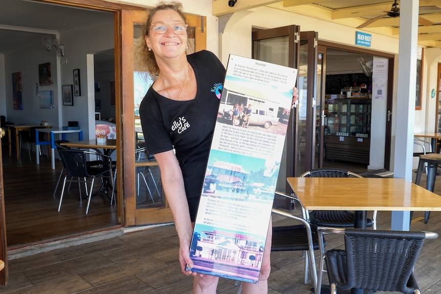 A woman holding a poster of historic photos in front of a cafe.
