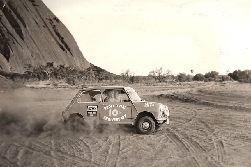 Jack Murray driving a Mini Minor car on sand at Uluru.