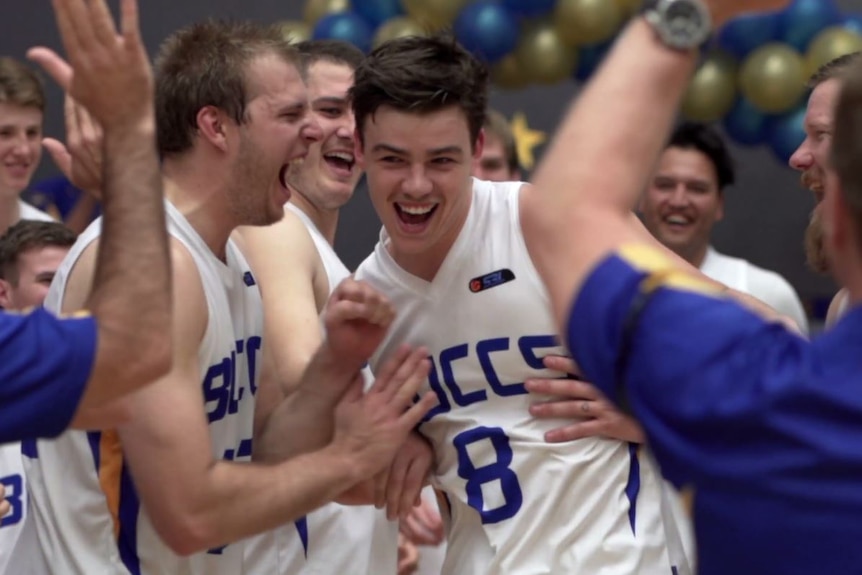 A young male basketballer smiles as he runs through his team mates.