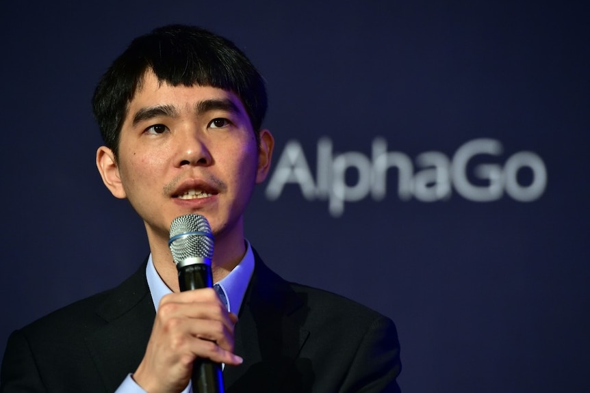 Lee Se-Dol holds a microphone as he speaks with the AlphaGo logo behind him