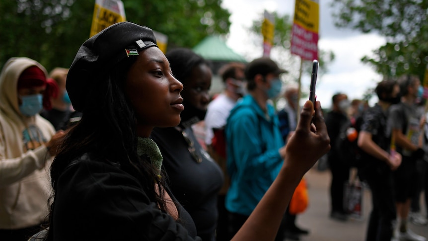 A woman in a black beret looks at her phone at a protest.