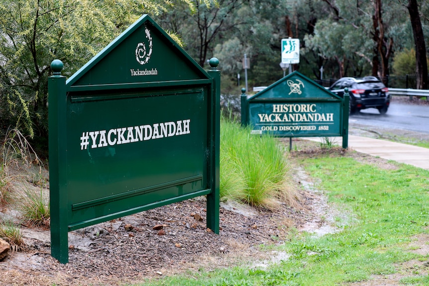 Two green signs welcoming motorists to Yackandandah with car passing on road