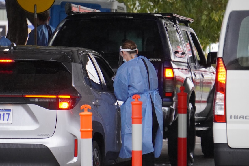 A woman takes a swab from a person in a car at a drive-through COVID testing clinic.