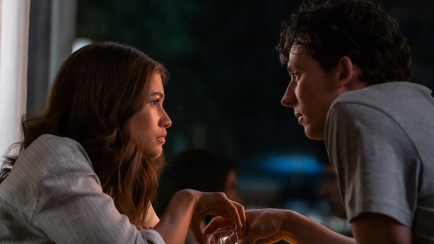 A film still of Zendaya and Josh O'Connor. It's night and they're leaning into each other, holding alcohol glasses.