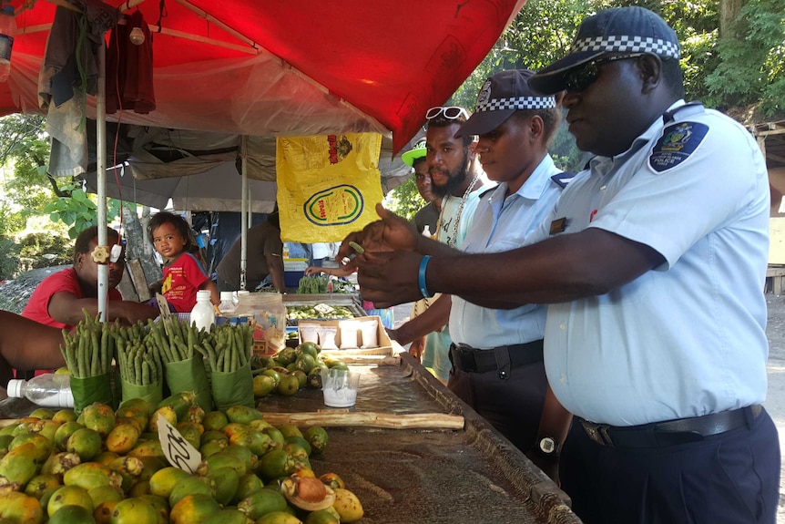 Uniformed solomon islands police officers speak to betel nut sellers at a market.