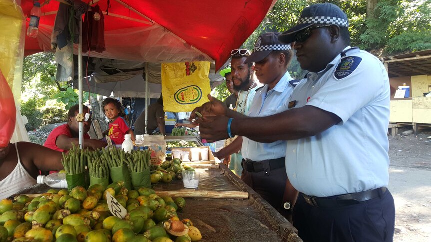 Uniformed solomon islands police officers speak to betel nut sellers at a market.