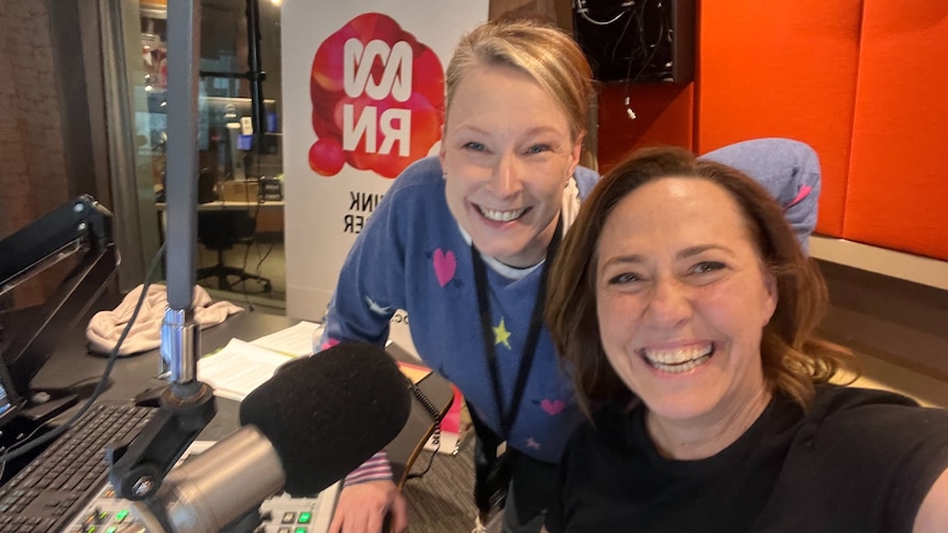 Two women in a radio studio smiling to camera.