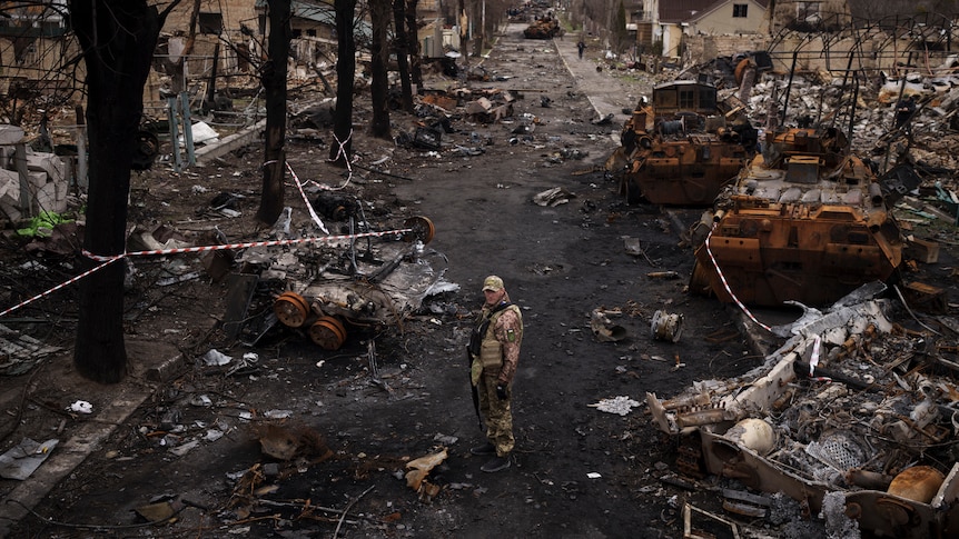 A Ukrainian serviceman stands amid destroyed Russian tanks.