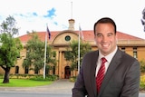  A man in a suit in front of a council building with two flags out the front