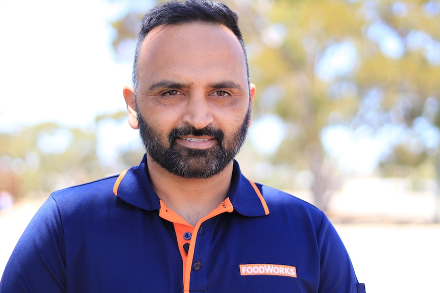 Man with beard and moustache, blue polo shirt, slight smile, background blurred.