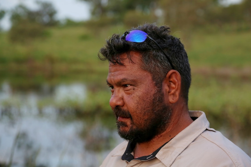 Side profile of a middle-aged Indigenous ranger against creek backdrop.