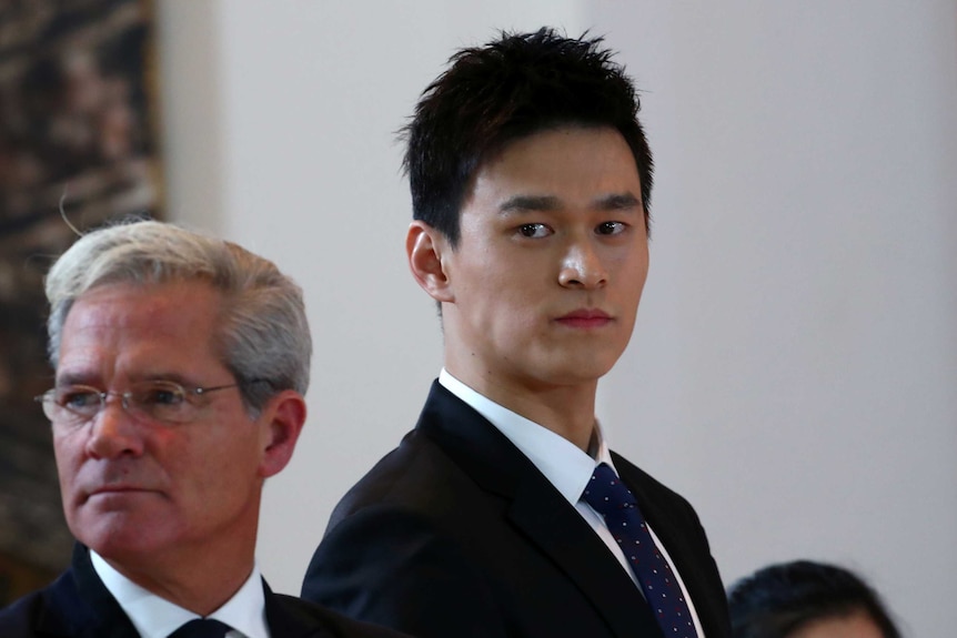Sun Yang standing in a court room in a black suit
