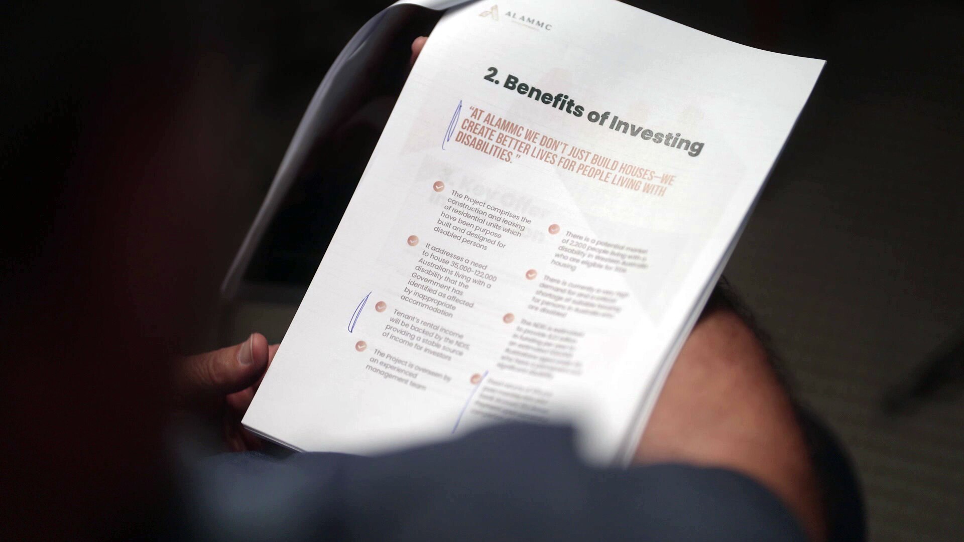 A person holds a series of documents printed on A4 paper stapled in the top left corner.