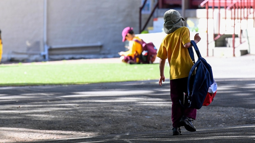 a young student walking into school carrying a school bag