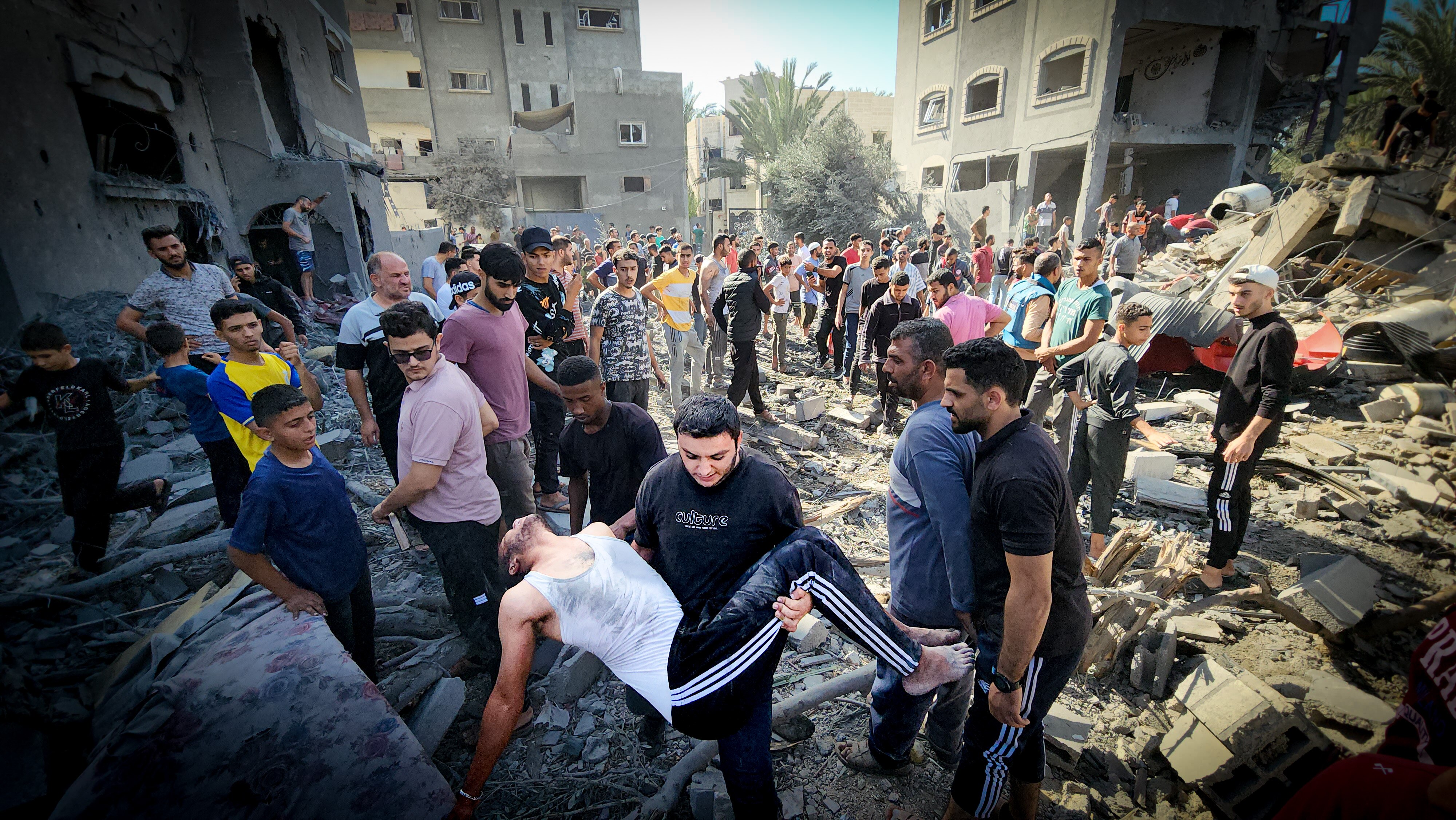 A man carries an injured man out of a bomb crater