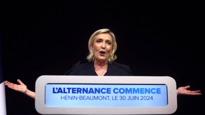 Marine Le Pen, blonde woman, stands at podium with arms out