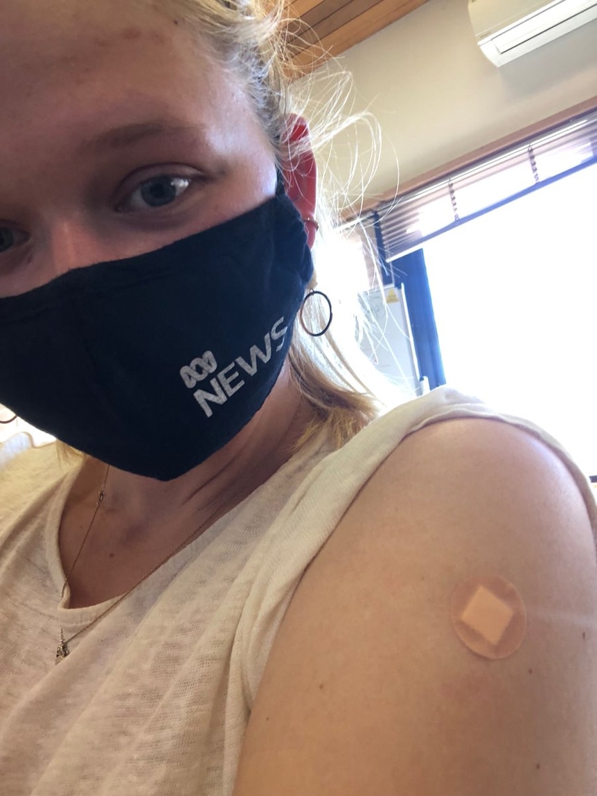 A blonde woman in a face mask takes a selfie of herself after receiving her COVID-19 vaccine