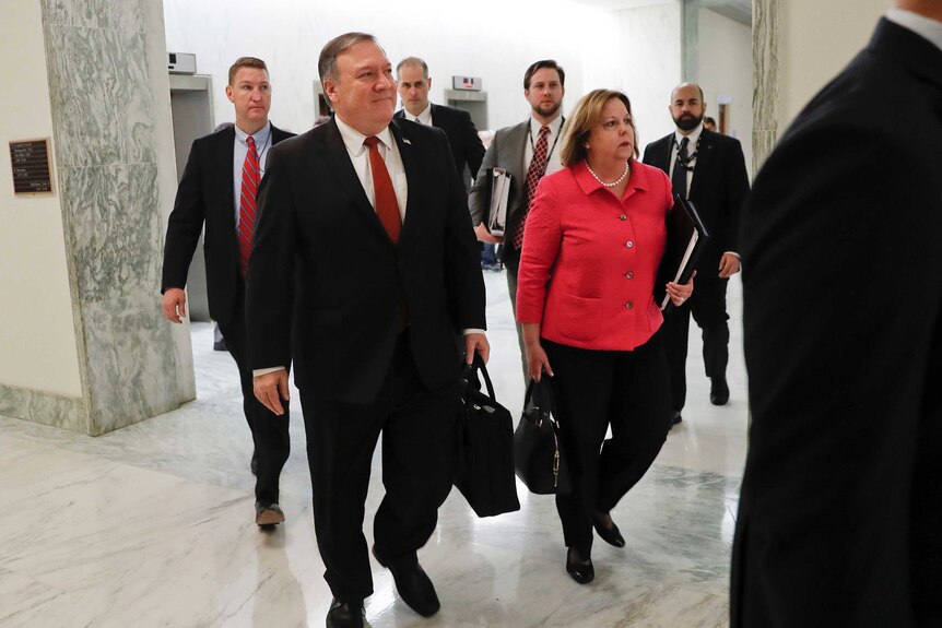 Mike Pompeo, among a group of people, walks to hearing room.