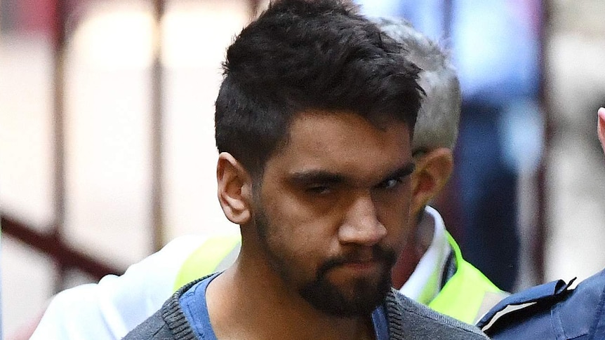 A man in handcuffs being escorted by a court security guard.