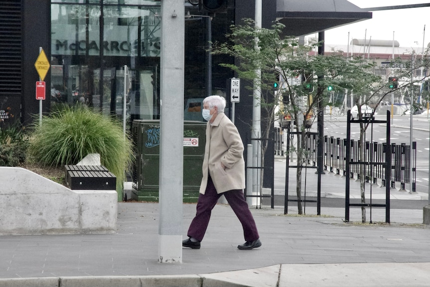 An elderly lady wearing a face mask walks along a street in Newcastle.