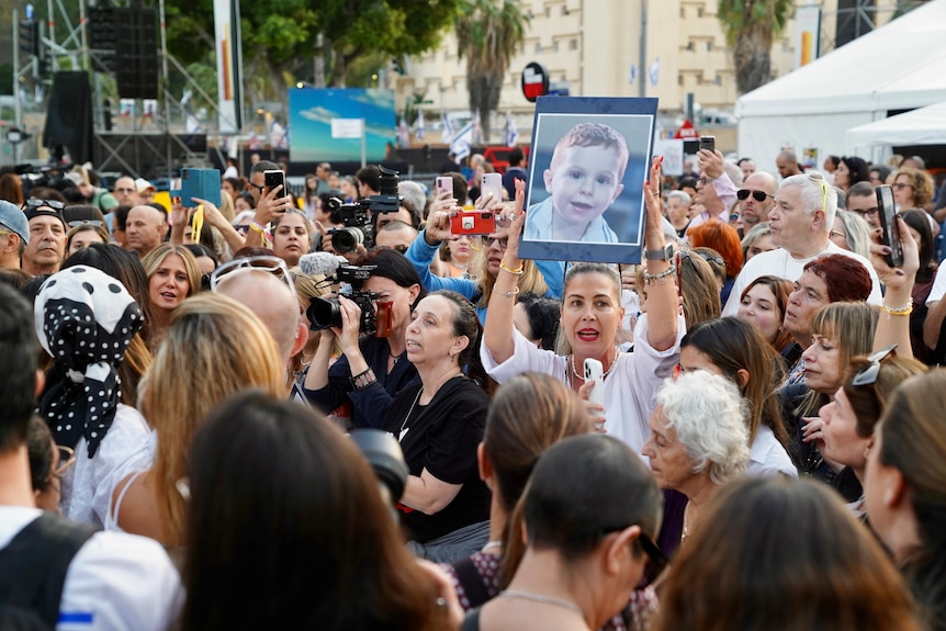 A crowd of people with one woman in the middle holding up a picture of a young child
