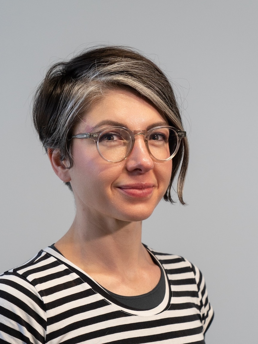 A young, dark-haired woman with blonde streak at the front wears glasses and a black-and-white striped T-shirt.