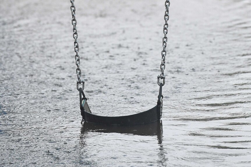 A children's swing sits in flooded waters at a playground on the Gold Coast,