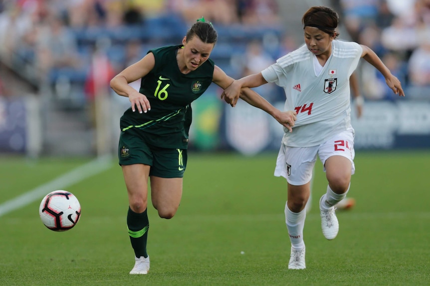 Hayley Raso runs down the line alongside a defender with her sleeves rolled up.