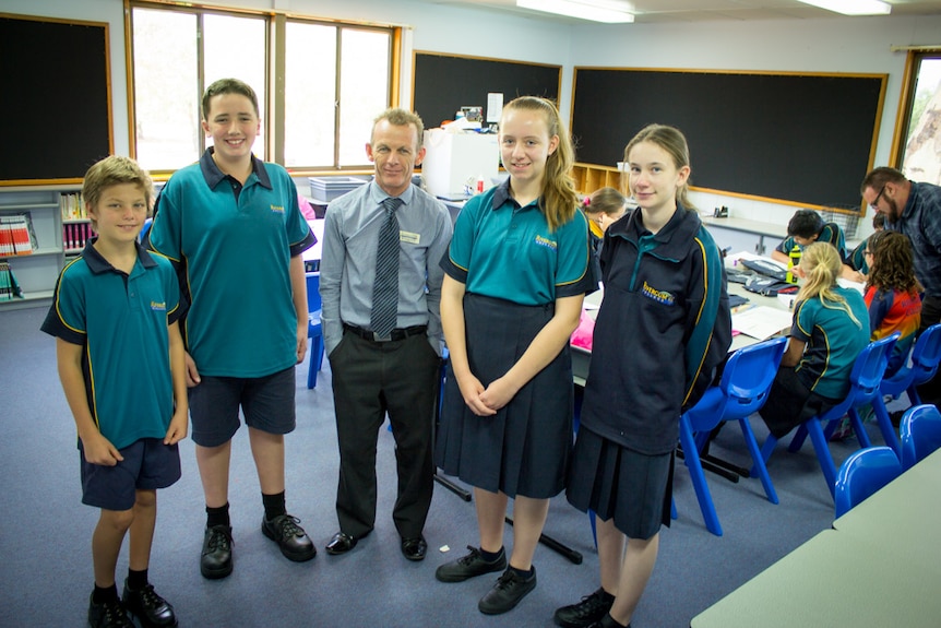 Rivergum College principal Gregg Smith standing with students Clay, Nick, Kelly and Isabella while other students work at desks.