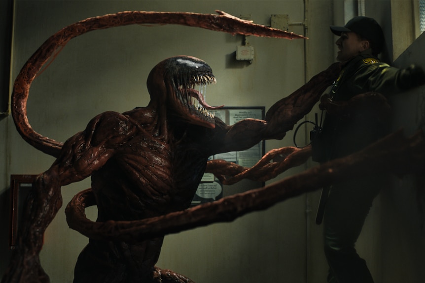 A dark muscular and slimy monster with razor-sharp teeth and many jagged sword-like arms pins a man in cap and jacket to a wall.