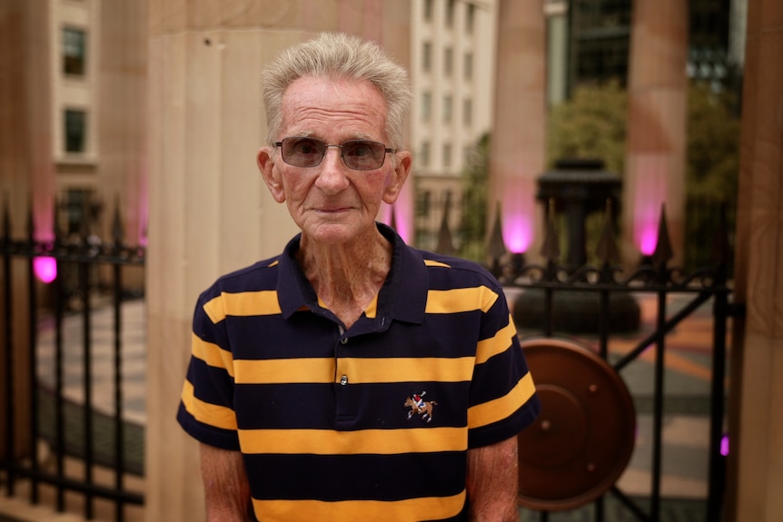 Len Mcleod looking directly at the camera. In the background are the illuminated columns of the Brisbane War Memorial.