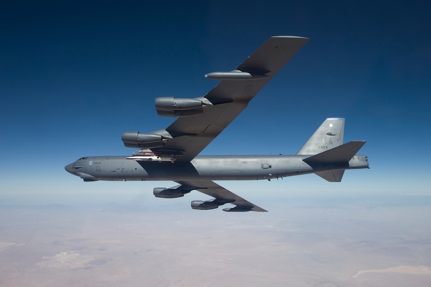 Photo of a B-52 bomber flying over the desert under a blue sky.