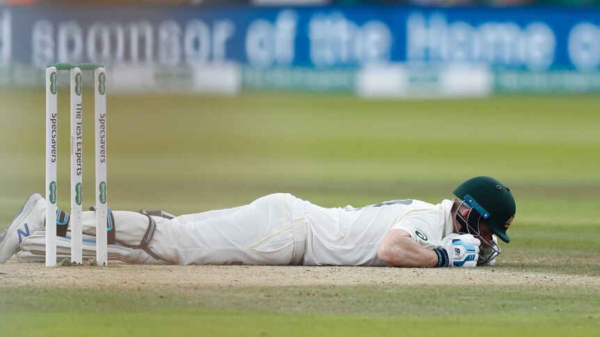 Steve Smith lies face down on the pitch with his helmet on.