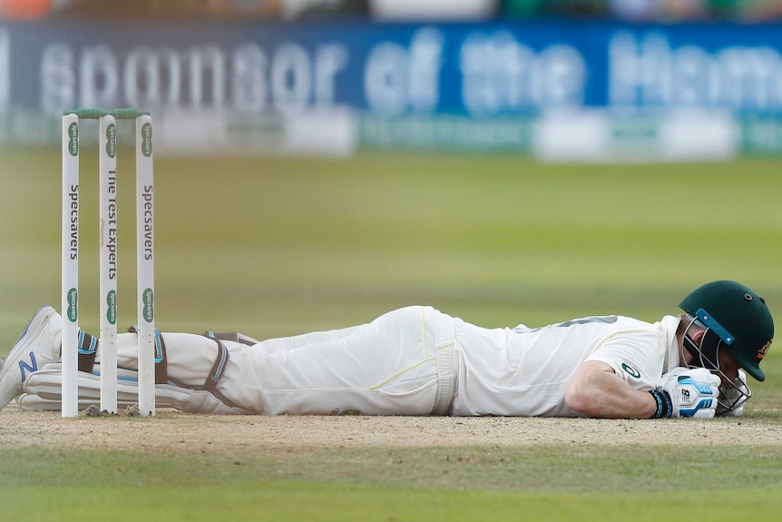 Steve Smith lies face down on the pitch with his helmet on.