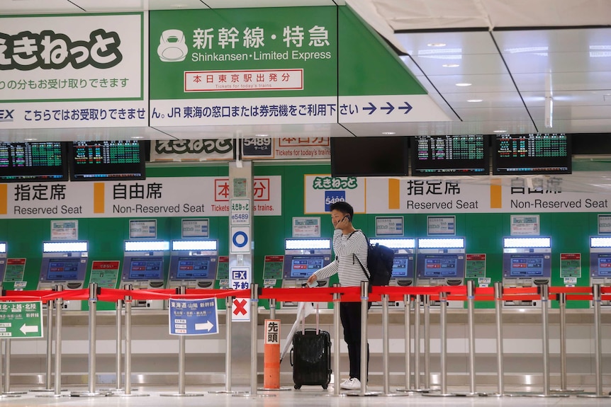 A man stands with a suitcase at an empty counter at Tokyo Station.