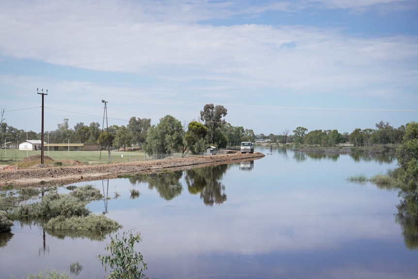 A truck drives along a levee next to water and tennis courts