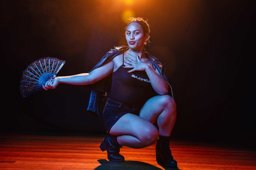 A dramatic wide colour portrait of Kilia Tipa holding a fan and posing in front of dark background.