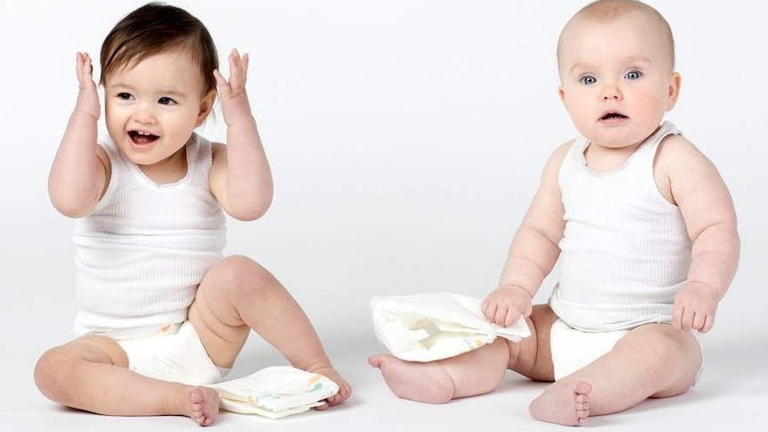 two babies sit on the floor and play with nappies