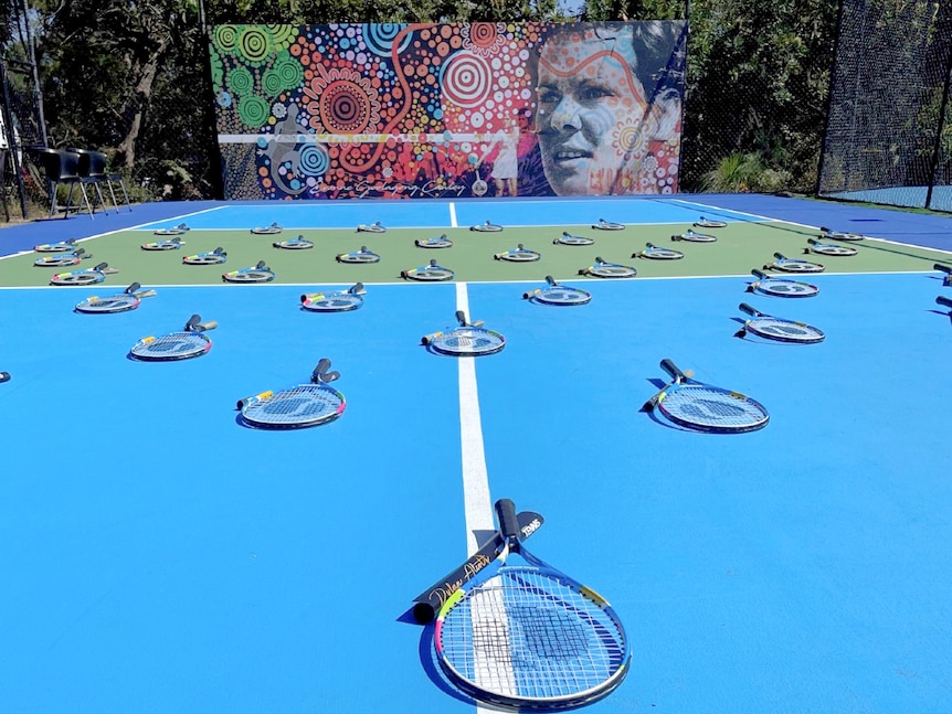 An indigenous mural at the back of a tennis court.