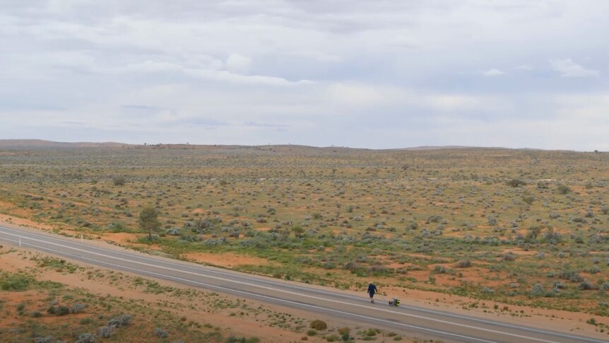 A man walking with a cart along a road in the desert near Broken Hill. 